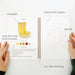 Open notebook with watercolor painting instructions and materials on a white background