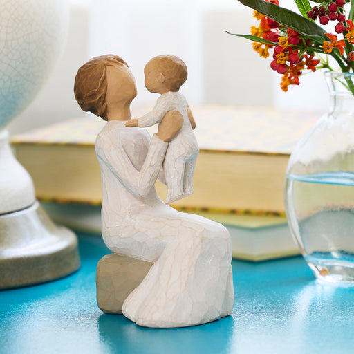 Figure of seated older woman in cream dress, holding baby up in the air