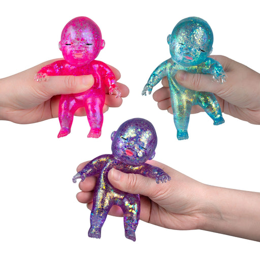 Three iridescent baby figurines held by hands against a white background