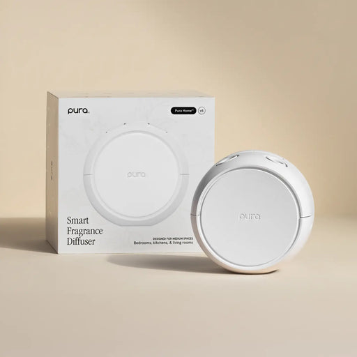 A white Pura Smart Fragrance Diffuser shown next to its white retail box on a warm beige background.