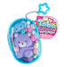 Purple plush bear with colorful pom-poms in a blue gachapon capsule, next to Tabalicious packaging.