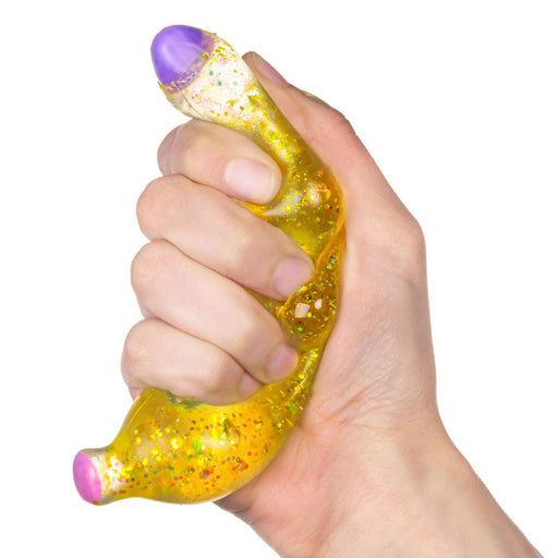 A hand squeezing a translucent yellow sensory stress toy filled with glitter, featuring a purple textured top and a pink bottom, on a white background.