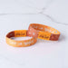 Two orange wristbands with 'God is good' and 'Tap to Pray' text on a light gray background