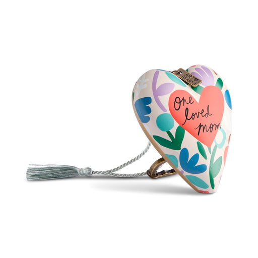 A heart-shaped wooden keepsake box with a colorful floral pattern and a pink heart that reads 'one loved mom' in black script. It has a silver tassel and clasp, photographed on a clean white background.