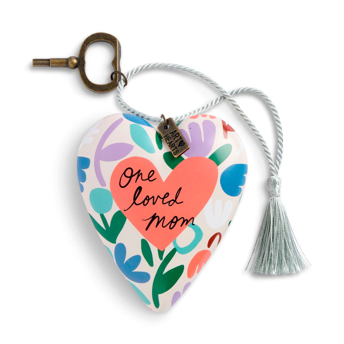 Heart-shaped ceramic keepsake plaque with a floral pattern, featuring a coral heart in the center with the words 'One loved Mom' in black script. The plaque is attached to a white rope with a tassel and a brass key ring, and a small 'Made in PA' tag is hanging from it.