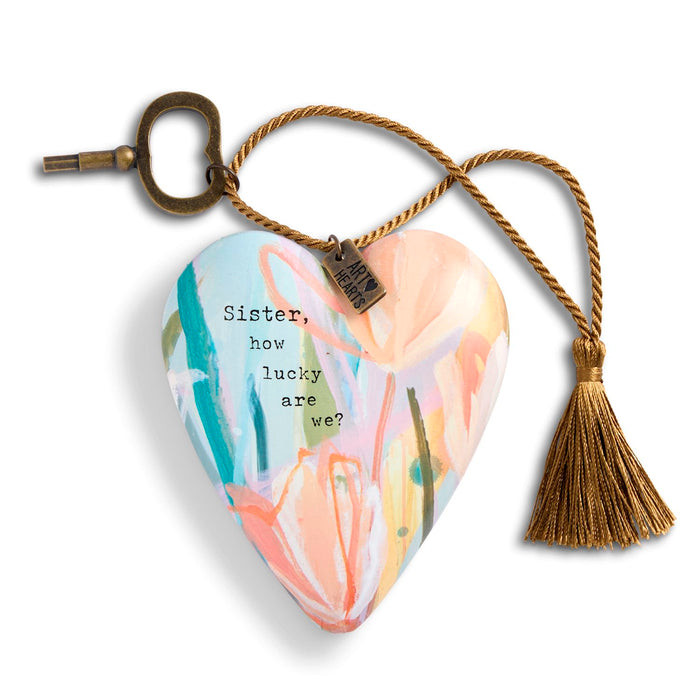 Heart-shaped keychain with 'Sister, how lucky are we?' text and tassel on a white background