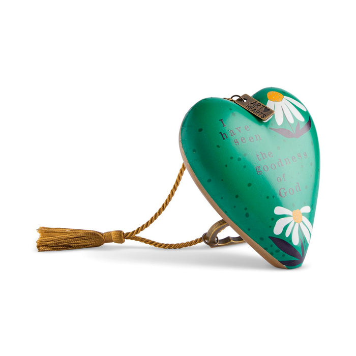 A heart-shaped wooden prayer box with a green finish, decorated with white daisy flowers, gold lettering that reads 'I have seen the goodness of God', and a gold tassel on a white background.