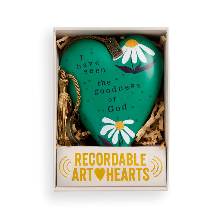 A heart-shaped green ornament with white daisy illustrations and the text 'I have seen the goodness of God' inside a gift box with a tassel and a card reading 'RECORDABLE ART HEARTS'.