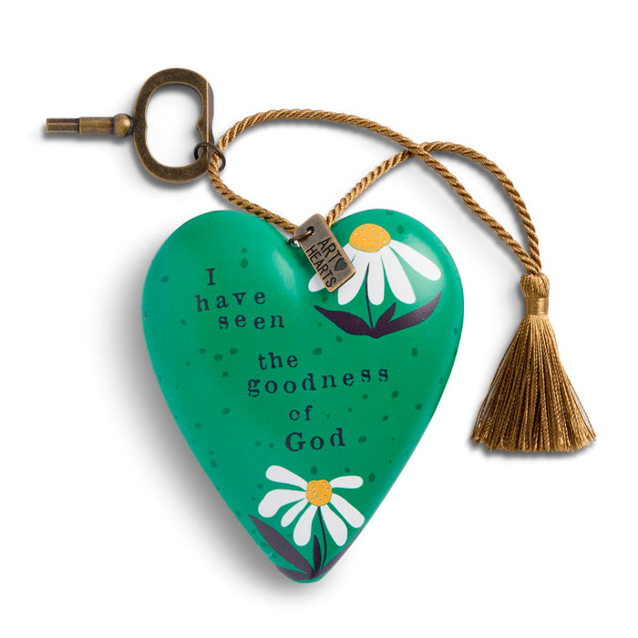 A green heart-shaped wooden prayer tag with white daisy illustrations and the printed text 'I have seen the goodness of God'. It features a brass keyhole loop at the top, a gold-colored hanging cord, and a matching tassel.