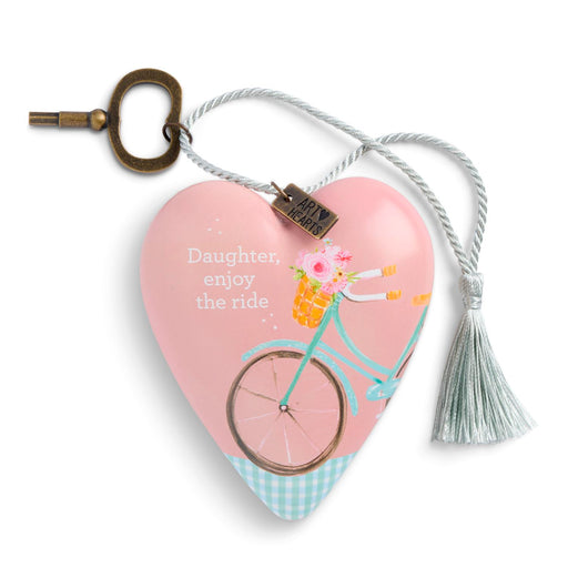 A heart-shaped keepsake box with a pink lid featuring a bicycle illustration and the text 'Daughter, enjoy the ride.' It has a silver rope with a tassel and a brass key, shown on a white background.