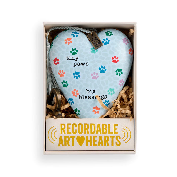 A heart-shaped ceramic pet memorial ornament in a gift box. The ornament is light blue with a white pet-print pattern and colorful paw prints, featuring the text 'tiny paws big blessings'.