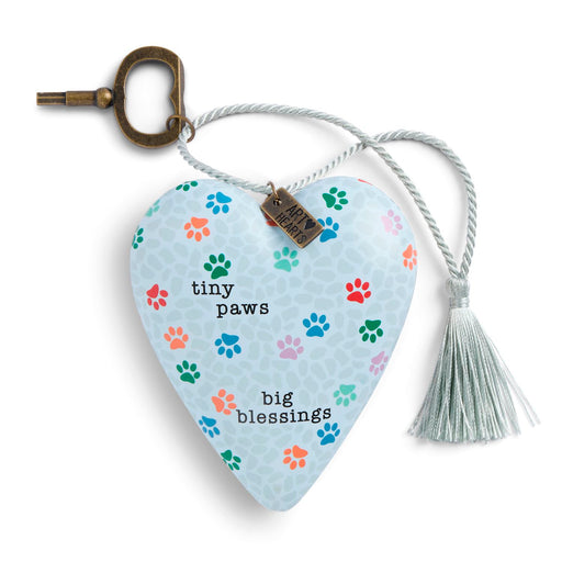 A heart-shaped guitar pick keychain with a light blue background, decorated with colorful paw prints and the text 'tiny paws big blessings'. It features a silver-colored hanging rope with a tassel, a brass key ring, and a small metal tag.