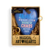 A heart-shaped blue ornament with multicolor text reading 'FAMILY WHERE LOVE BEGINS IN CHAOS NEVER ENDS', presented in a gold gift box with shredded paper filler and a tassel.
