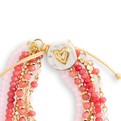 Stack of pink beaded bracelets with gold accents and a heart charm on a white background