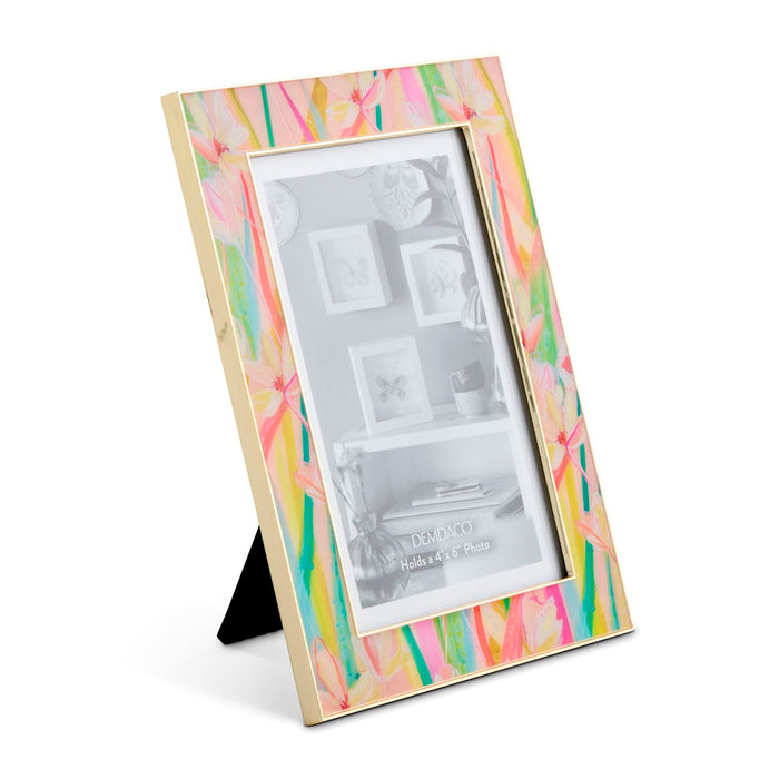 A vertical picture frame with a gold-toned inner border and a colorful abstract floral design in pink, yellow, green, and blue on the outer frame, shown standing on a small black easel against a white background.