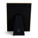 The back view of a black picture frame with a gold-toned border and a matching black triangular stand, featuring a white signature on the stand, set against a plain white background.