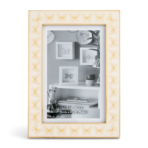 A rectangular picture frame with a cream-colored border featuring a repeating gold butterfly pattern, holding a black-and-white photo of wall frames and decor.