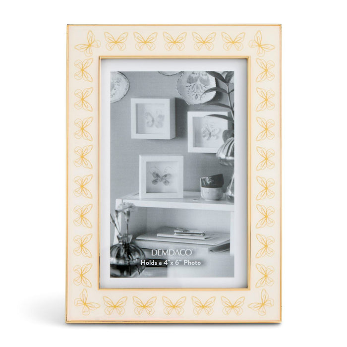 A rectangular picture frame with a cream-colored border featuring a repeating gold butterfly pattern, holding a black-and-white photo of wall frames and decor.