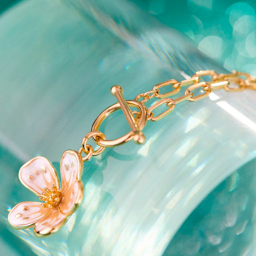 Gold bracelet with a floral charm on a light blue background