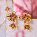Gold floral earrings on a marble surface with a blurred pink background