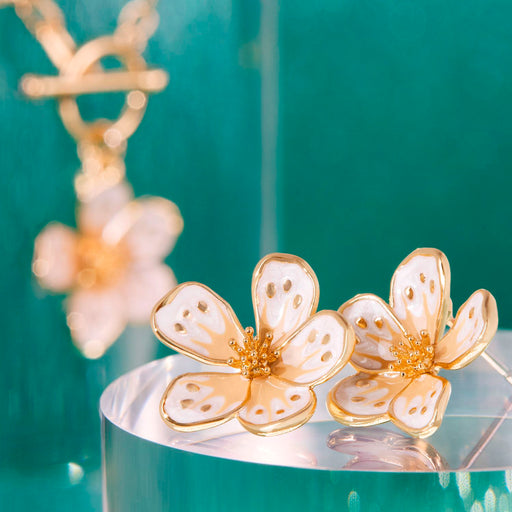Gold floral earrings on a clear stand with a teal background