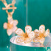 Gold floral earrings on a clear stand with a teal background