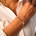 Close-up of a person wearing a gold bracelet with floral designs on a light background.