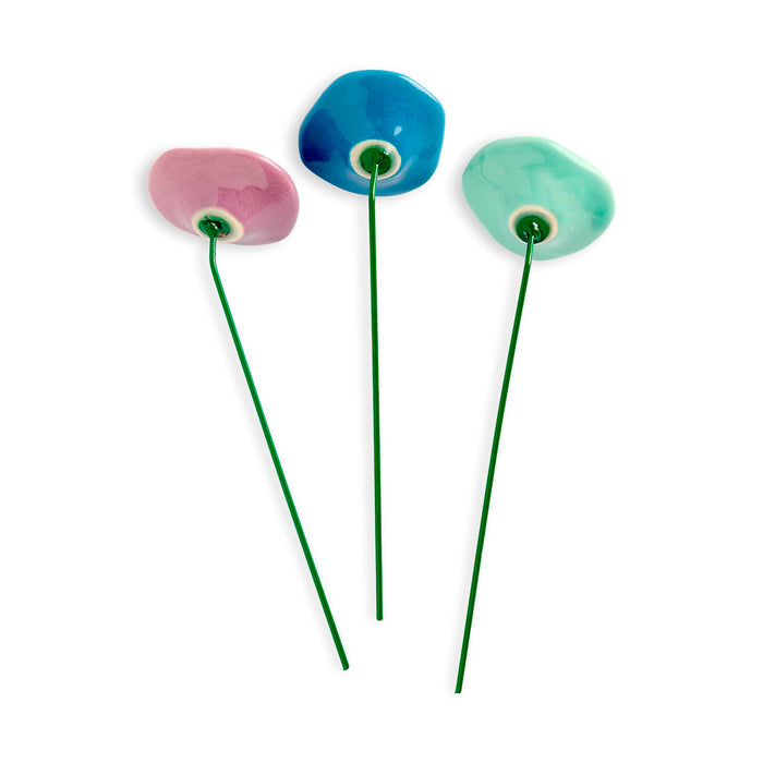 Three colorful ceramic flowers on green stems against a white background