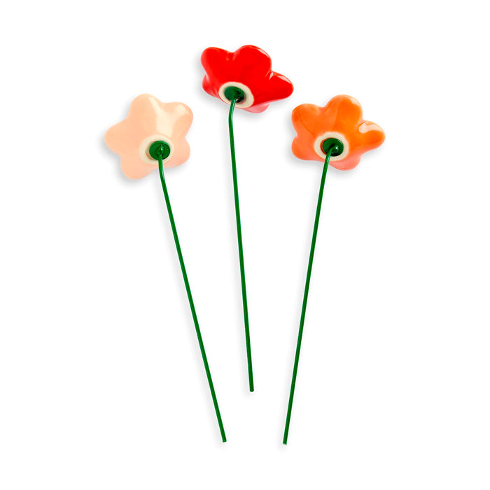 Three colorful ceramic flowers on green stems against a white background