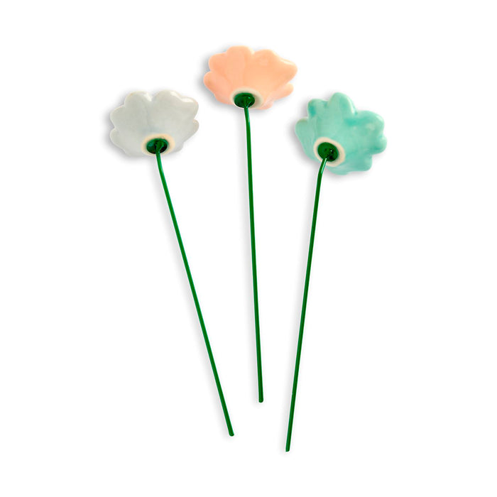 Three ceramic flowers on green stems against a white background