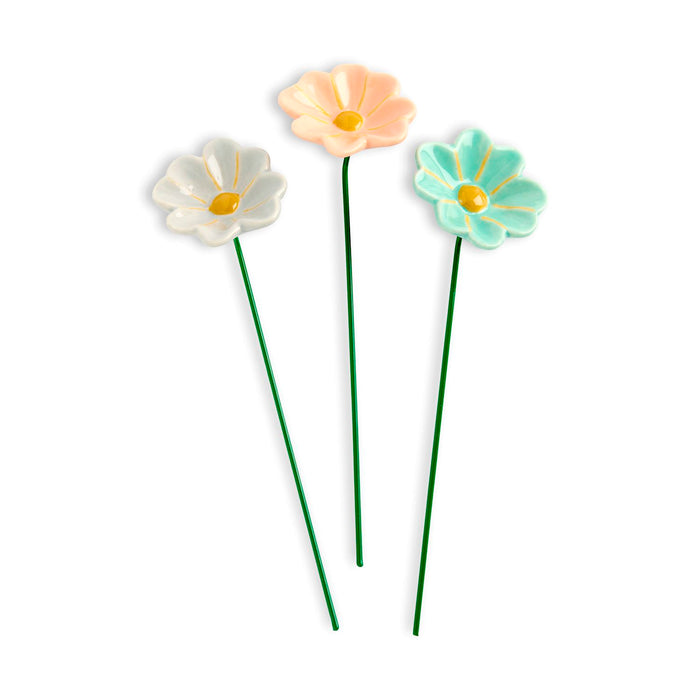 Three colorful ceramic flowers on green stems against a white background