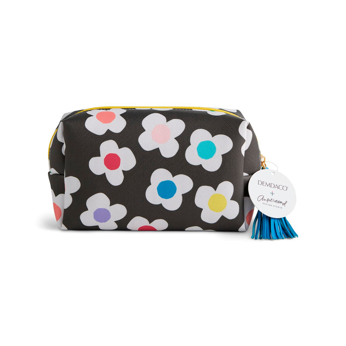 A rectangular cosmetic pouch with a black background and a white daisy pattern featuring colorful flower centers. It has a gold zipper, a blue tassel, and a white circular tag that reads 'DE'MEACO x Charmander'.