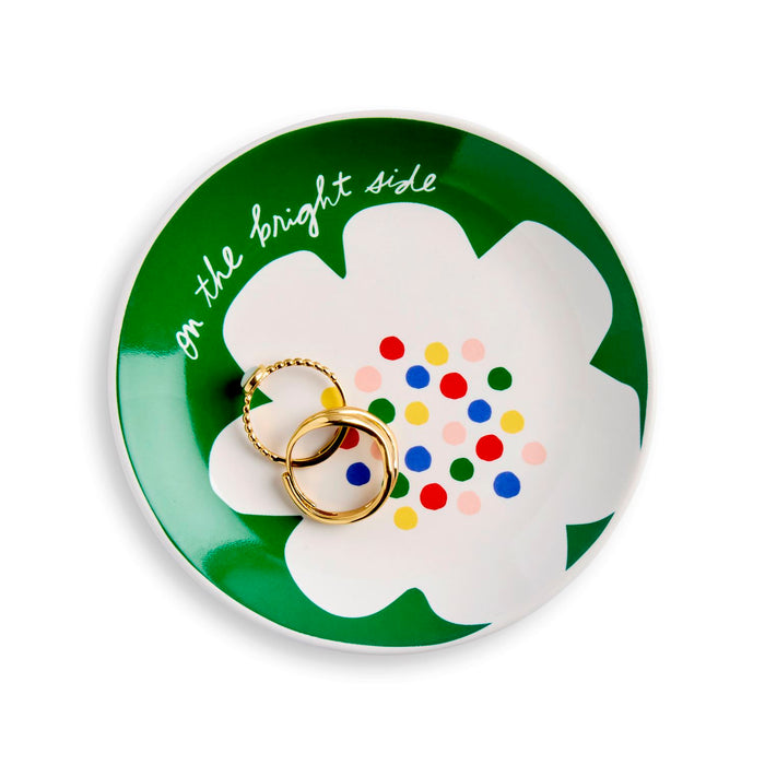 Round green trinket dish with a white flower design and colorful polka dots, featuring two gold rings.
