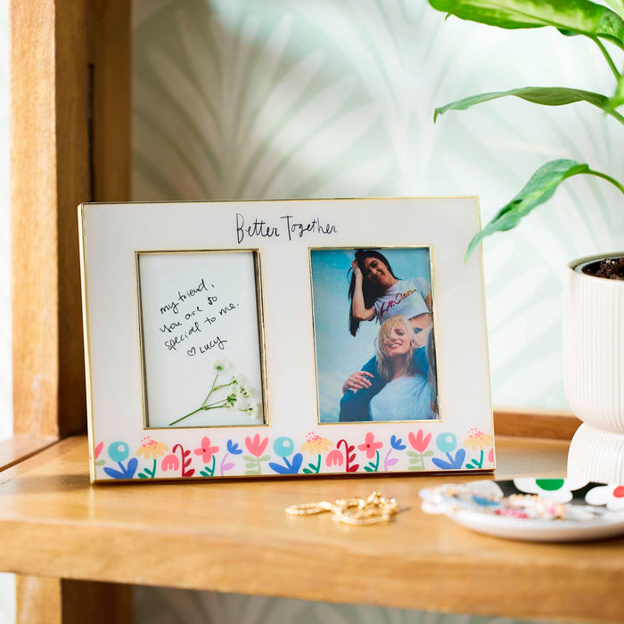 Two-photo frame with floral design on a wooden surface with a plant in the background