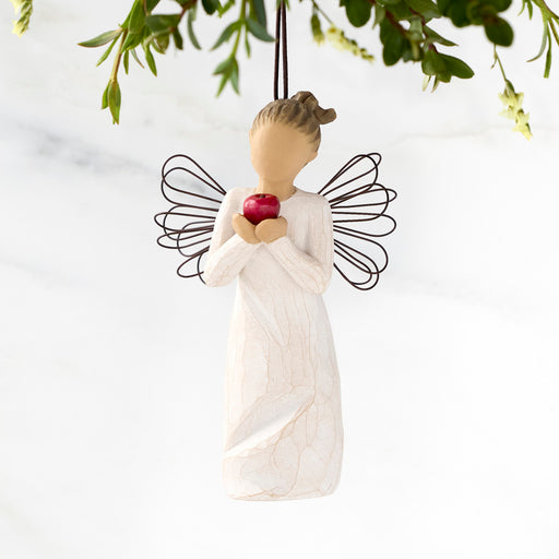 Angel figurine holding a red apple with green leaves in the background