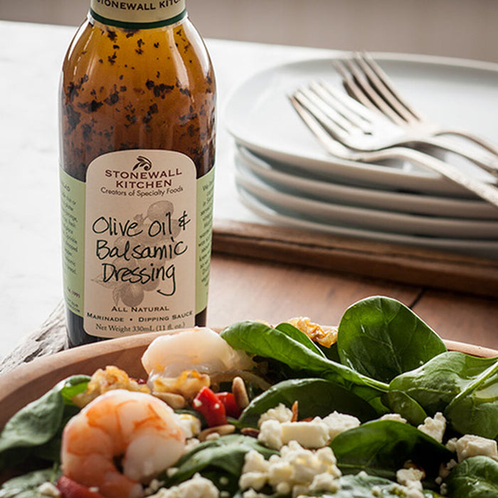 Bottle of Stonewall Kitchen olive oil and balsamic dressing next to a salad with shrimp and cheese.