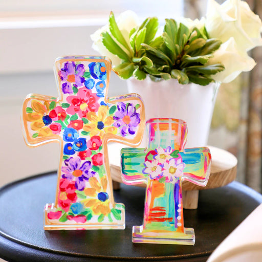 Colorful cross-shaped decorative items on a table with a plant in the background
