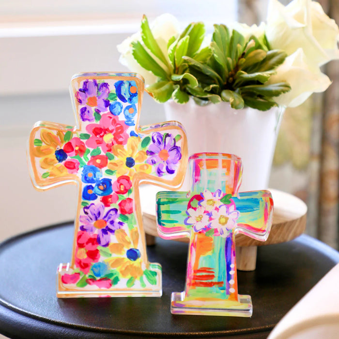 Colorful cross-shaped decorative items on a table with a plant in the background