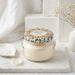 Jar of cream with a decorative lid on a marble surface, surrounded by white flowers and a vase.