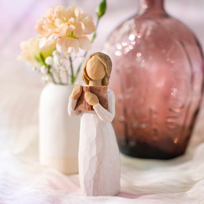 Decorative figurine of a woman holding flowers next to a vase with flowers on a soft surface.