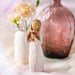 Decorative figurine of a woman holding flowers next to a vase with flowers on a soft surface.