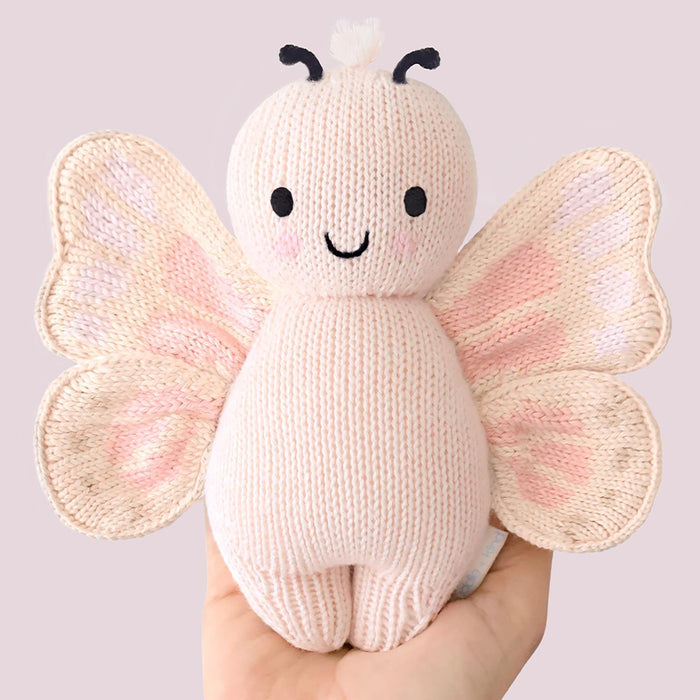 Knitted butterfly toy held by a hand against a plain background
