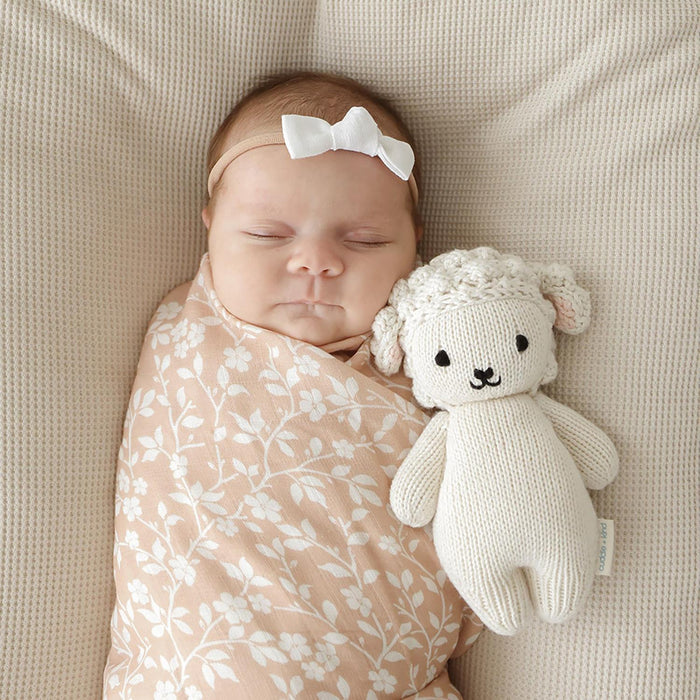 Newborn baby sleeping with a white knit lamb toy on a beige blanket