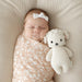 Newborn baby sleeping with a white knit lamb toy on a beige blanket