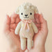Knitted teddy bear with a pink bow held in hands against a beige background
