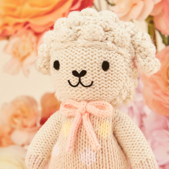 Knitted toy sheep with a pink bow on a floral background
