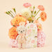Knitted teddy bear with a floral gift box and bouquet of flowers on a beige background