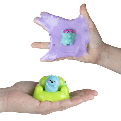 Taba-Licious Couch Potato puppy squish toy stretched across a hand with another puppy sitting on a green couch below.