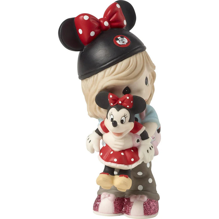 A collectible figurine of a blonde girl wearing a black Minnie Mouse hat with a red bow and holding a small Minnie Mouse doll, set against a plain white background.