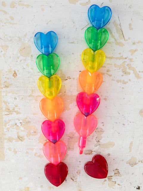 Colorful heart-shaped objects arranged in a vertical line on a textured surface.